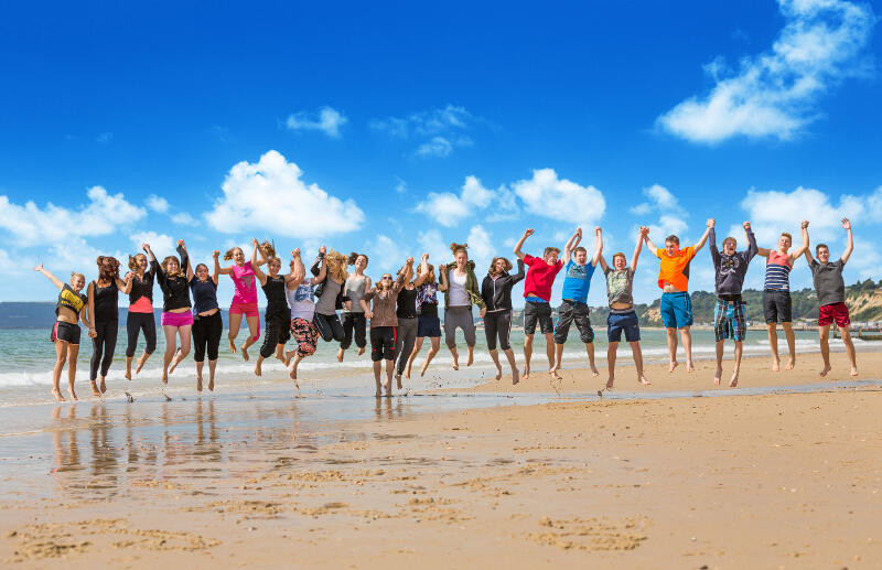 Groepsfoto van jongeren die springen op het strand op vakantiekamp