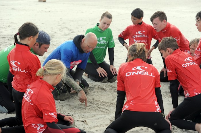 Een groep deelnemers van het surfkamp Nederland 13 jaar krijgt les op het strand van een surf instructeur