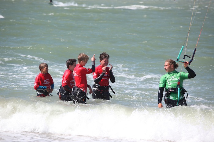 Deelnemers van surfkamp zeeland krijgen kitesurfles in het water van een professioneel kampbegeleider