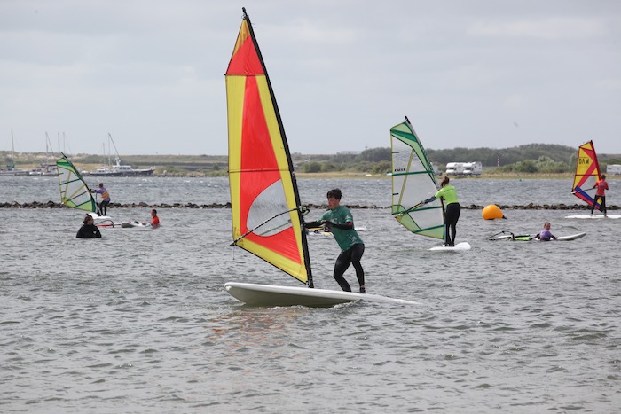 Deelnemers van een surfkamp Nederland 13 jaar zijn individueel aan het windsurfen