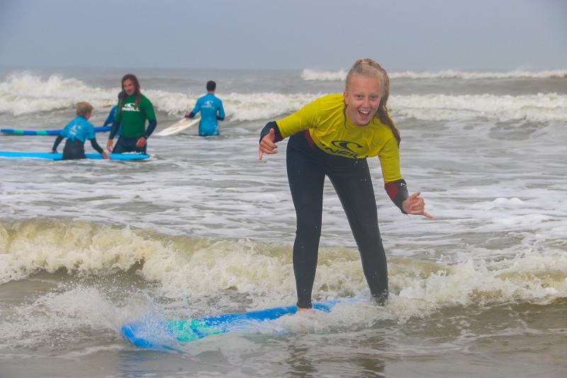 Deelnemer van het surfkamp Zeeland surft zelf over de golven naar het strand en ze neemt een coole pose aan