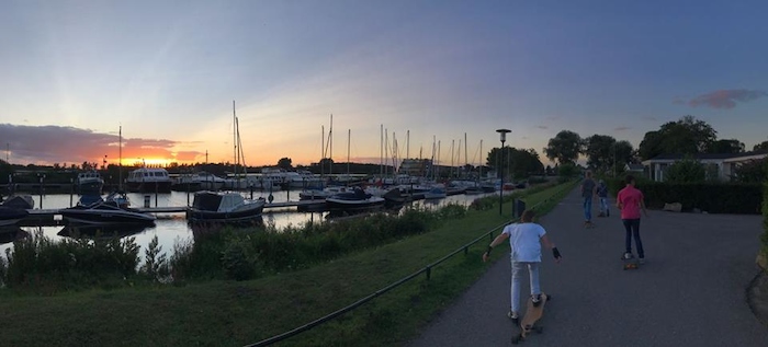 jongens skaten op de weg langs de boten bij zonsondergang op watersport kamp in de biesbosch