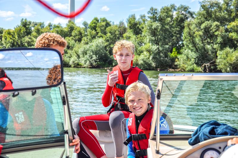 Deelnemers tijdens watersportkamp zitten op boot in water