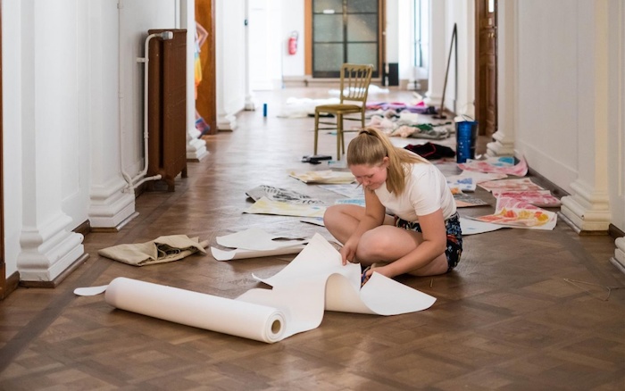 Meisje knipt papier op de grond tijdens het fashionkamp.