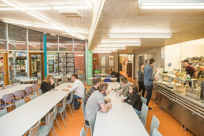 Deelnemers aan jongerenkamp zitten in refter en eten.