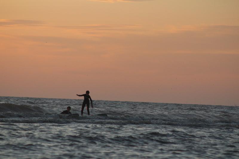 Deelnemers van sportkamp surfen in de zee bij zonsondergang