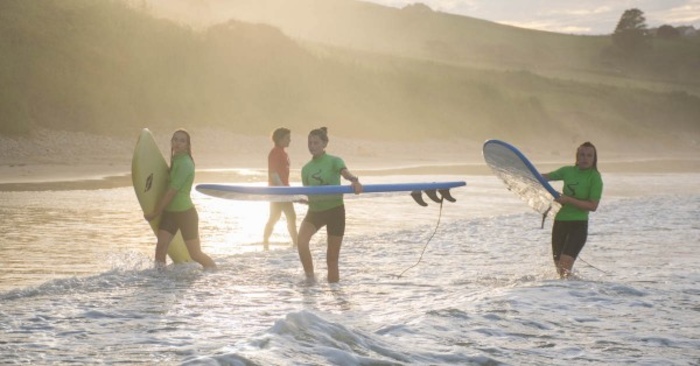 Meisjes wandelen de zee uit met hun surfboard.