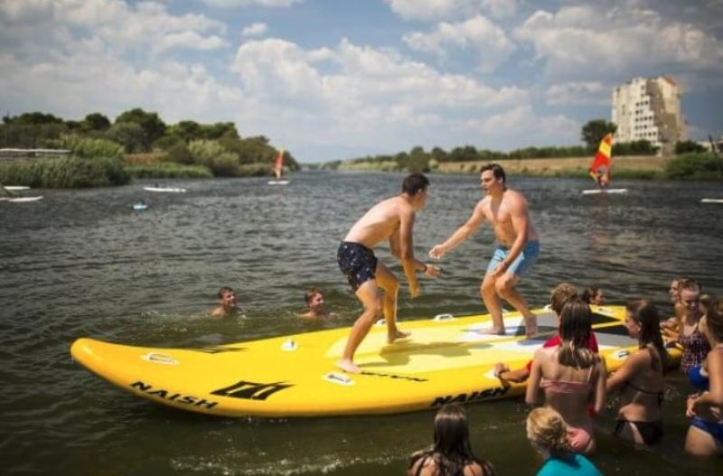 twee jongens staan op groot supboard en doen een spel op zomerkamp spanje watersportvakantie