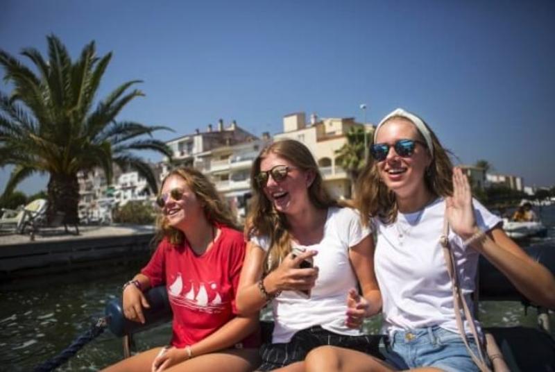 drie meisjes met zonnebril zitten op een boot te lachen op zomerkamp spanje watersportvakantie