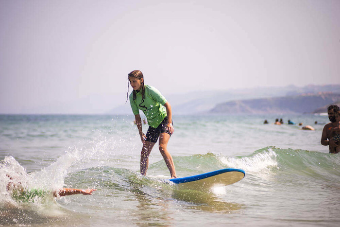 Een meisje staat op haar surfboard tussen de golven in Spanje tijdens een jongerenreis spanje surfkamp