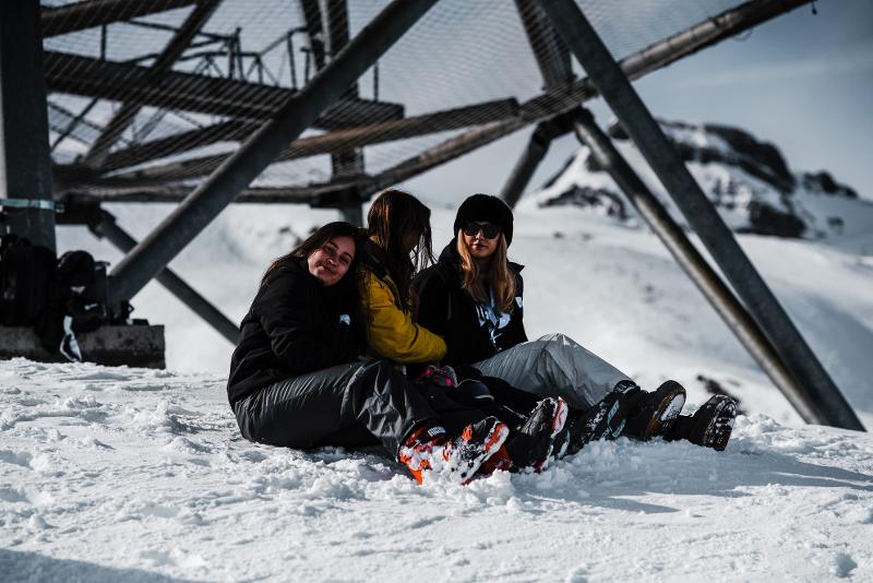 Drie meisjes zitten in de sneeuw op groepsreis skivakantie