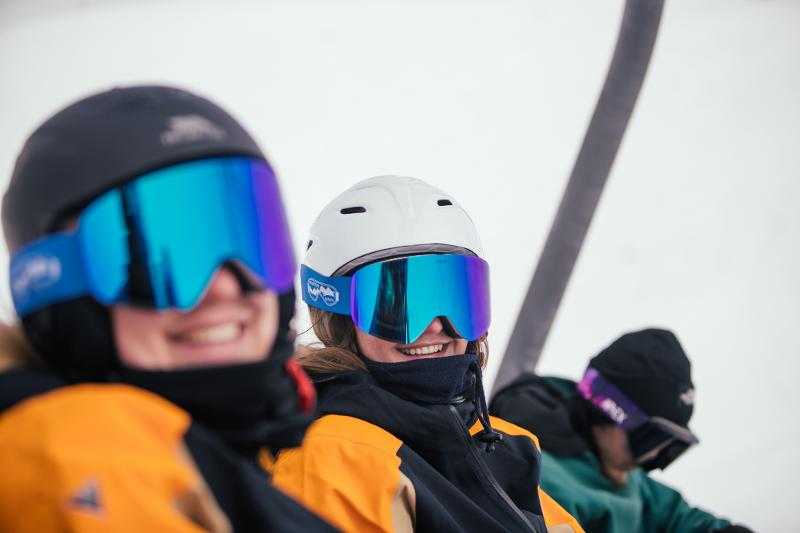 Drie jongeren met skibrillen lachen naar de camera op groepsreis skivakantie