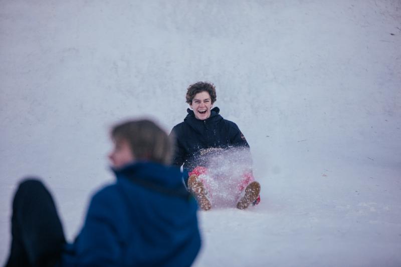 Een jongen op een poepslee in de sneeuw op groepsreis skivakantie