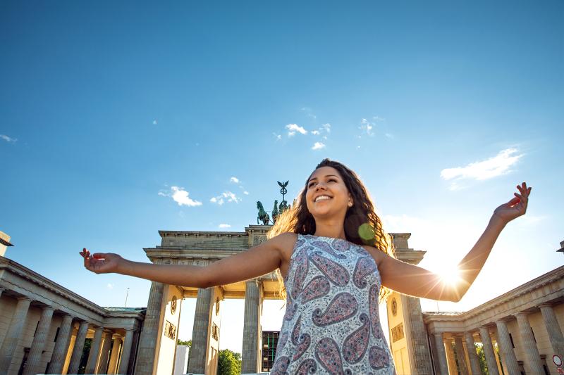 Een deelnemer van de taalcursus Duitsland vrolijk op de foto voor Brandenburger Tor in zonnig Berlijn
