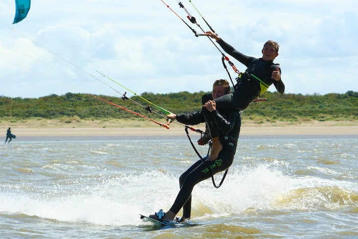 Een jongen zit op nek van een andere jongen tijdens het kitesurfen tijdens een kitesurfkamp