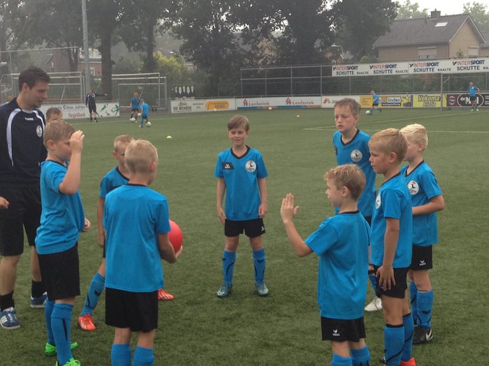 Deelnemers van voetbalkamp staan met coach op het veld in een cirkel