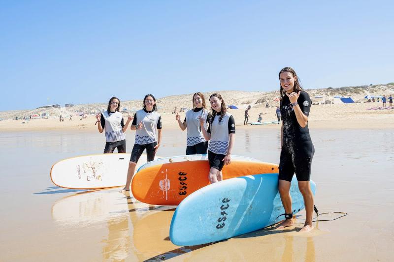 Vijf meisjes staan op het strand met hun surfplanken op surfkamp
