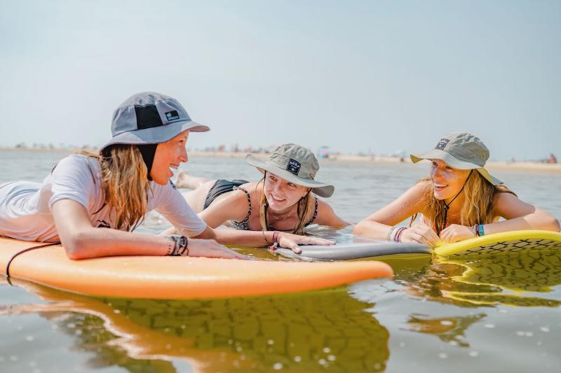 Drie meisjes liggen op hun surfplanken in het water op surfkamp