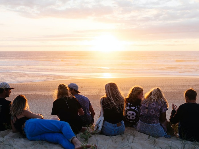 Jongeren zitten samen de zonsondergang te kijken.