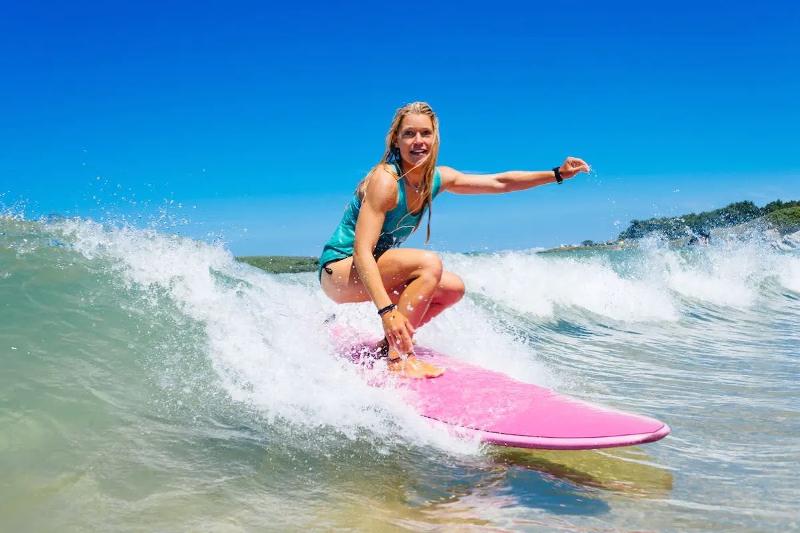 Deelneemster aan een surfkamp 14 jaar surft op de golven naar het strand toe