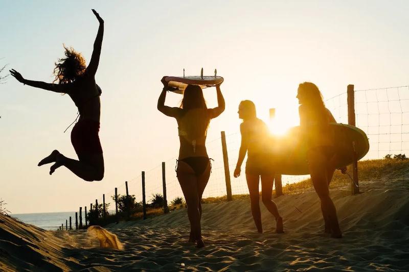 vier deelnemers van het surfkamp 14 jaar lopen met surfplanken richting het strand naar de zonsondergang