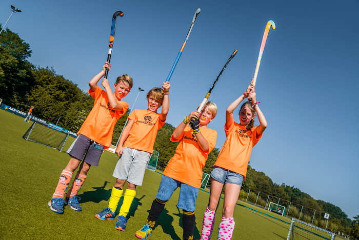 Kinderen houden hun hockeysticks in de lucht op sportkamp