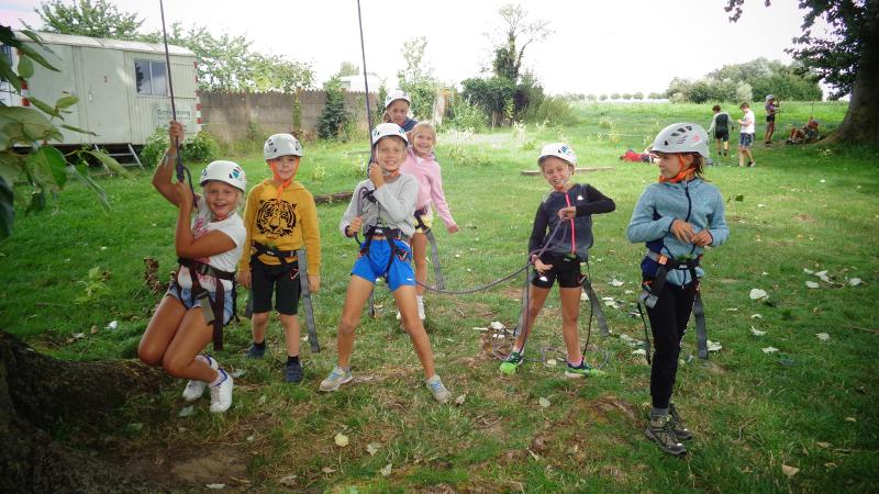 groepje kinderen staat met helm op een grasveld op tenniskamp