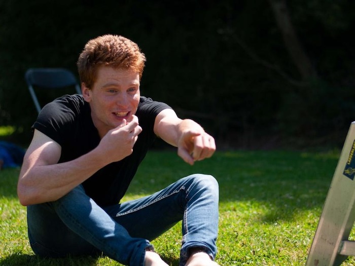 jongen zit op het gras en wijst in de verte tijdens theaterkamp in west-vlaanderen