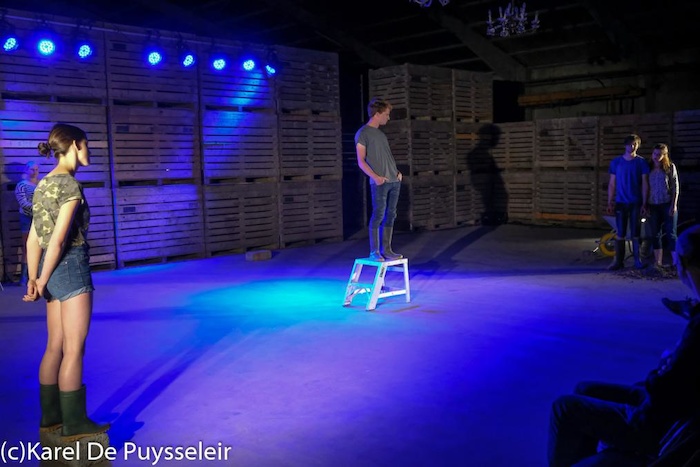 jongen staat op een kruk in blauw licht tijdens de voorstelling op theaterkamp in west-vlaanderen