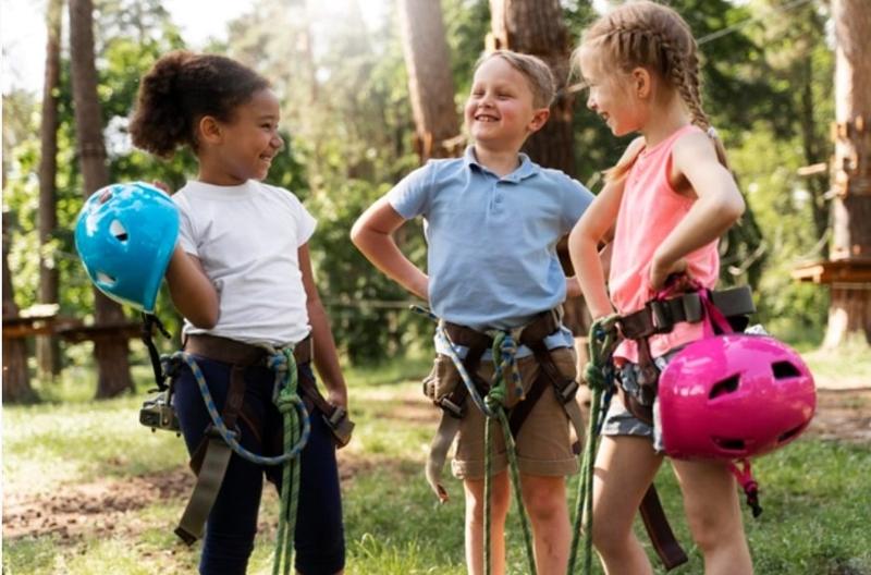 trois enfants équipés avec un casque pour faire de l'accrobranche en colo nature