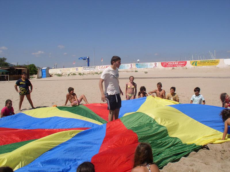 begeleider staat midden op gekleurd doek met kinderen eromheen tijdens een watersportkamp