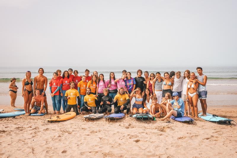 Alle deelnemers van een surf taalreis staan met elkaar op de foto op het strand