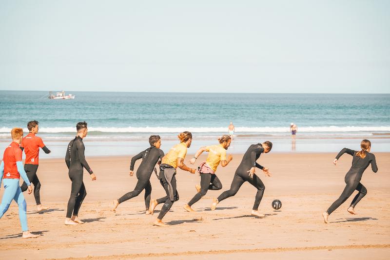 Deelnemers van een surf taalreis voetballen op het strand