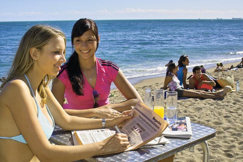 Twee meiden tijdens taalreizen jongeren lezen een krant op het strand