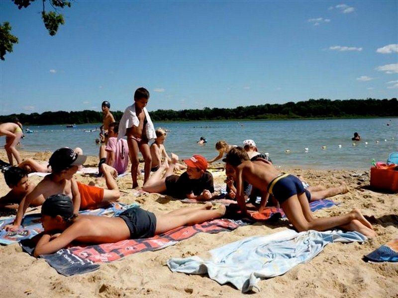 enfants sur le sable avec des casquettes près d'un lac en colonies de vacances surf