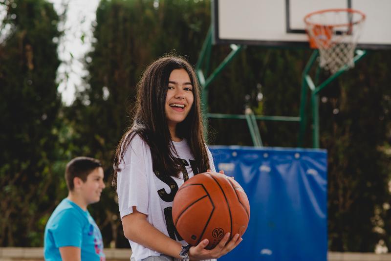 Een deelnemer van een taalkamp Engels jeugd houdt een basketbal vast