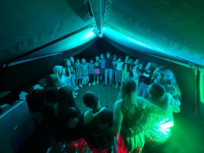 deelnemers staan in een cirkel in de tent in het donker op een natuurkamp jeugd in zandhoven