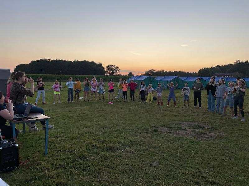 deelnemers staan in een cirkel en doen een spel tijdens zonsondergang op een natuurkamp jeugd in zandhoven