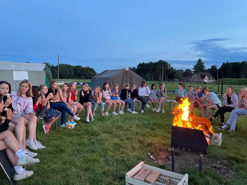 deelnemers zitten op bankjes bij de barbecue op een natuurkamp jeugd in zandhoven