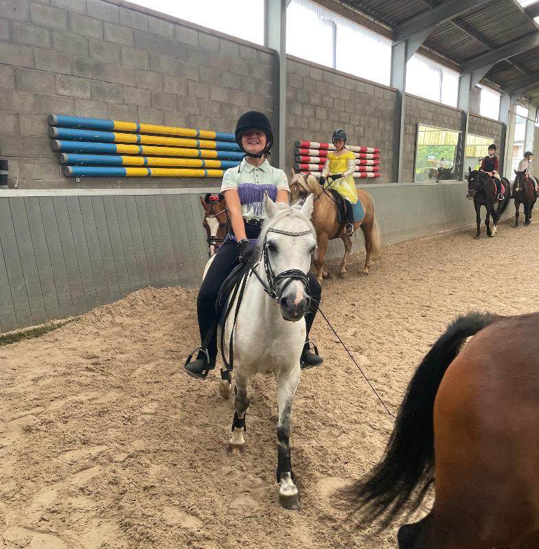 meisje zit lachend op een pony tijdens paardrijles op een natuurkamp jeugd in zandhoven