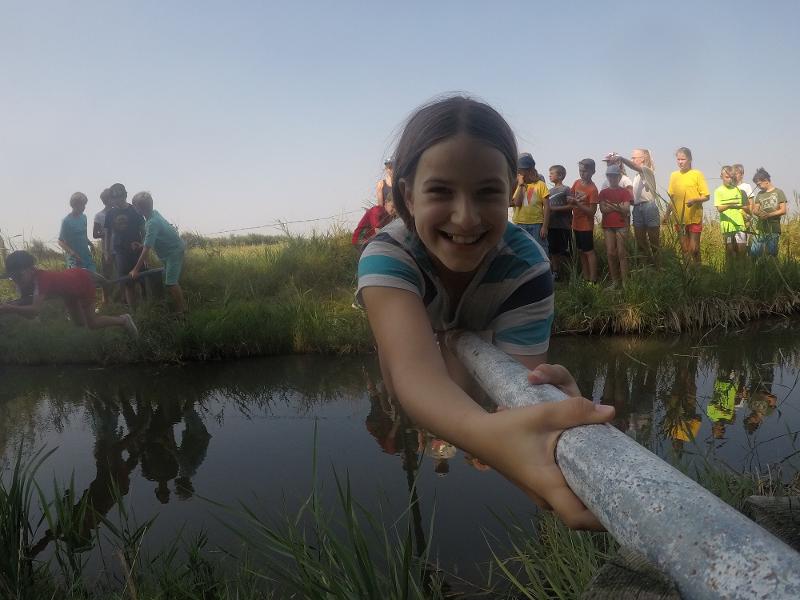 Meisje hangt horizontaal op een paal boven het water tijdens Natuurkampen