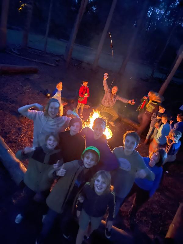 Kinderen staan rondom het kampvuur tijdens een avonturenkamp in belgie
