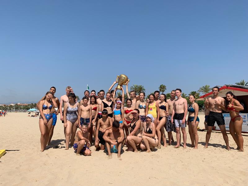 Een groepsfoto van deelnemers taalcursus Spaans Spanje op het strand met een trofee omhoog gehouden