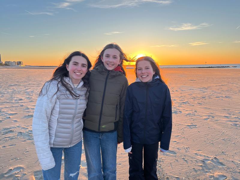 Drie deelnemers van groepsreis April staan op de foto op het strand met een ondergaande zon op de achtergrond