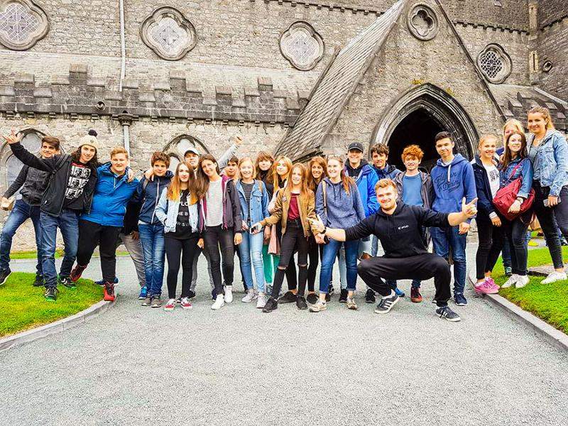 Een groep jongeren poseert voor een oud gebouw tijdens de taalreis in Ierland