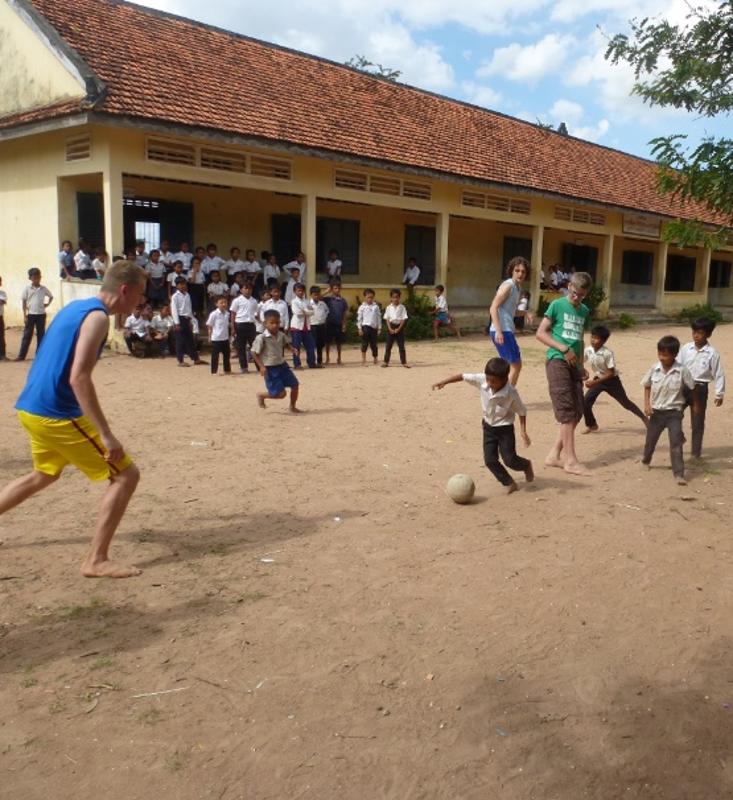 Deelnemers van een groepsreis Indonesië voetballen samen met lokale kinderen voor een schoolgebouw in Indonesië