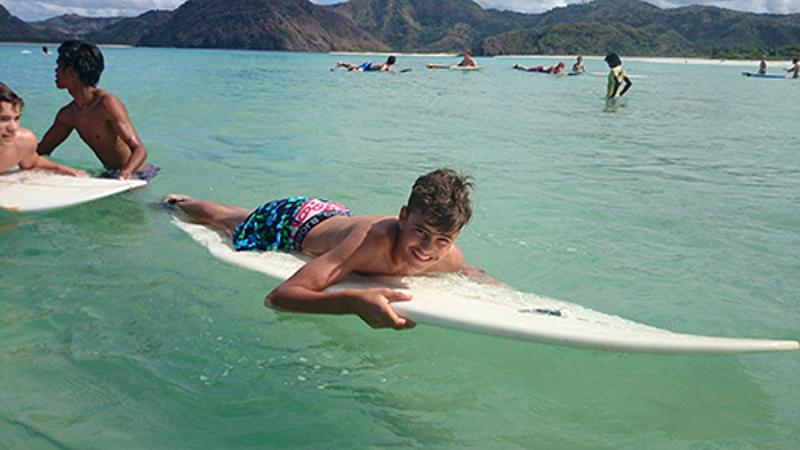 Deelnemer groepsreis Indonesië ligt op een surfplank in het kristalheldere water
