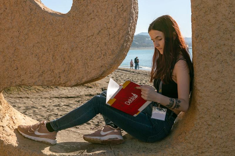 Een meisje zit op een bankje op het strand in een boek te lezen voor haar Spaanse cursus Spanje