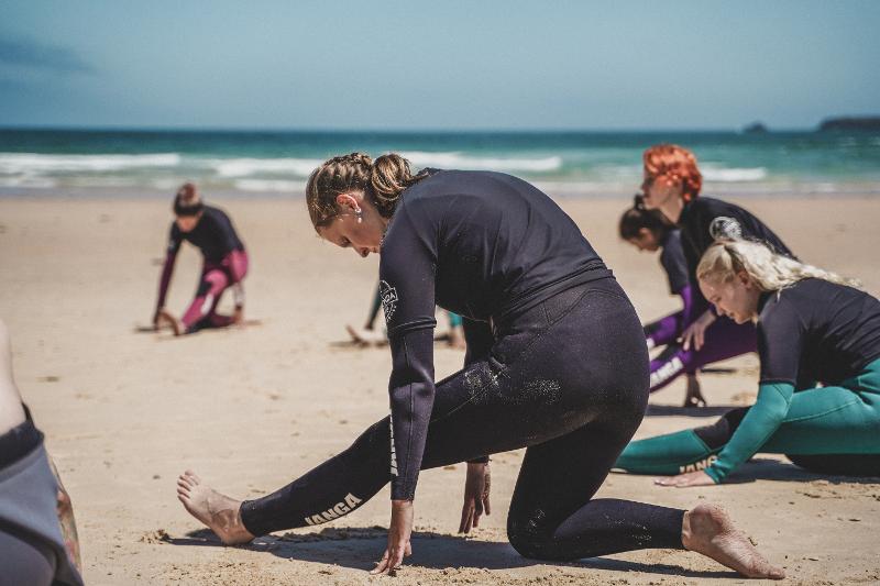 Meiden stretchen voordat ze het water op gaan tijdens een surf camp