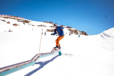 Jongen met snowboard glijdt over rails op skikamp